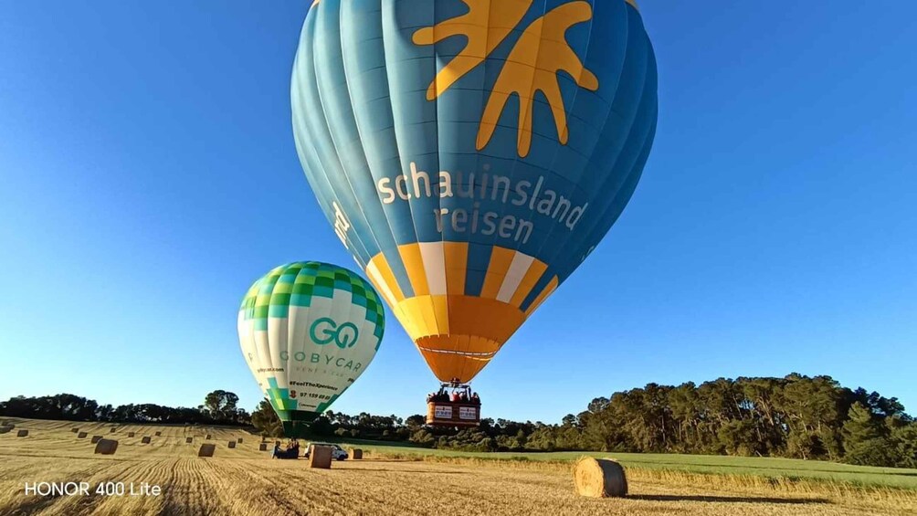 Two hot air balloons, one with 'schauinsland reisen' and the other with 'Go' branding, over a field with hay bales. 5