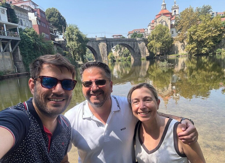 Three people taking a selfie with a historic bridge and river in the background. 1