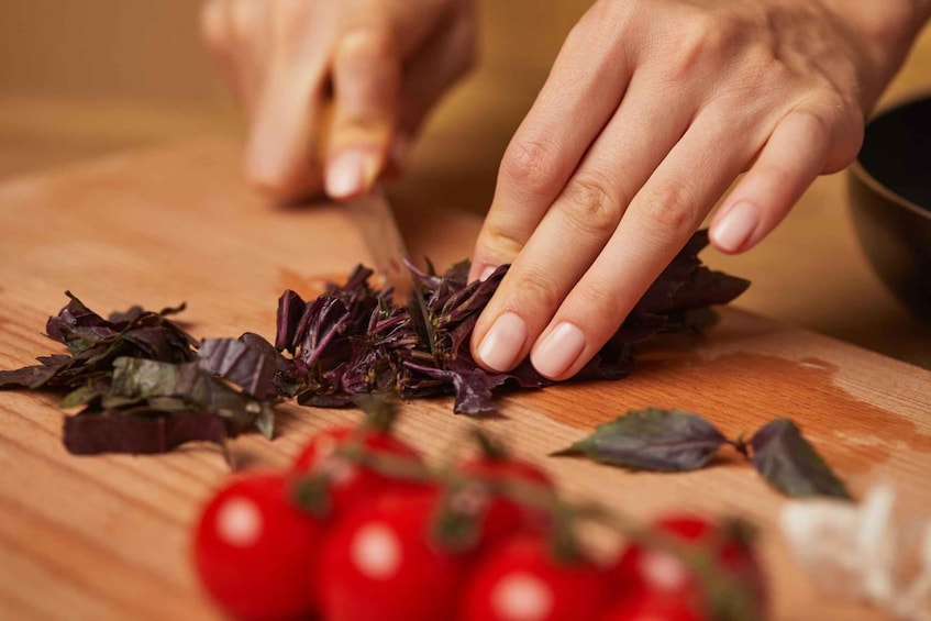 Hands chopping red tomatoes on a wooden cutting board. 3