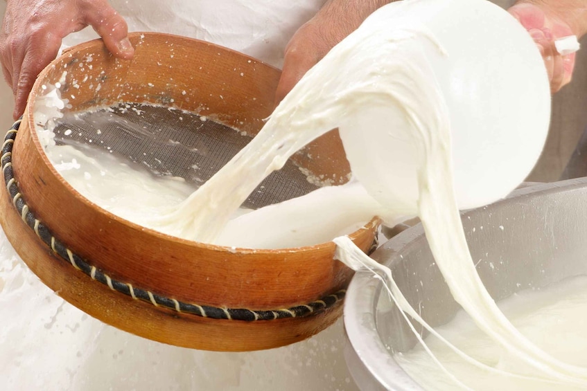 A person pouring a white liquid from a wooden bowl into a metal container. 1