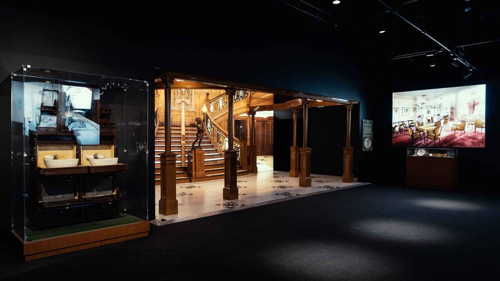 An exhibition with a wooden staircase, a glass display case, and a projection screen. 3