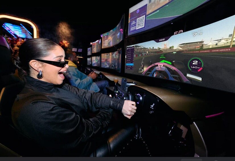 A person driving a racing simulator with multiple screens displaying a race track. 1