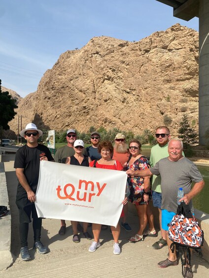 A group of people holding a banner with 'my tour' text, standing in front of a rocky mountain. 3