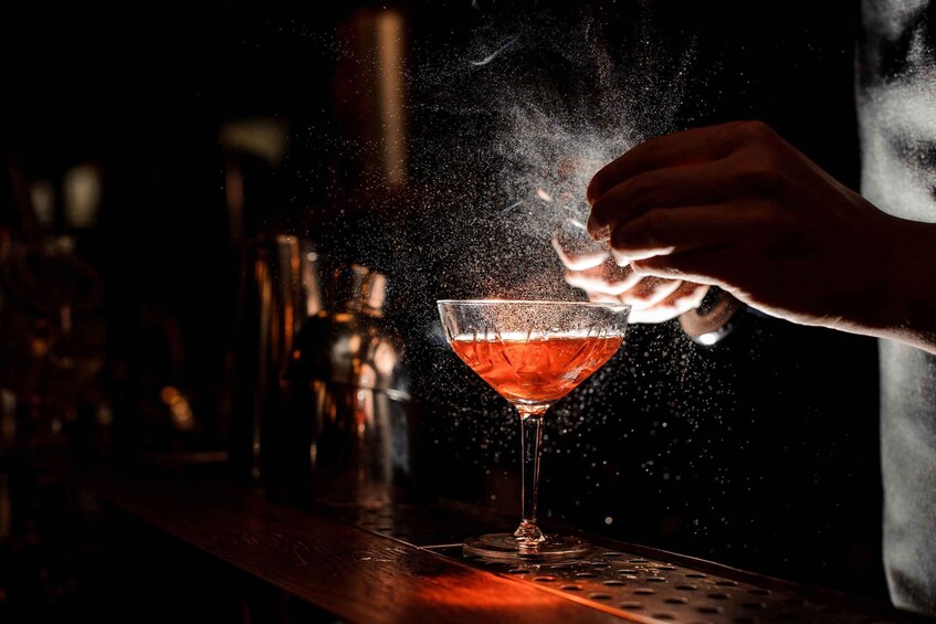 A hand sprinkling a powdery substance over a cocktail in a martini glass. 4