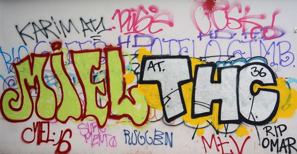 A wall covered with colorful graffiti, including the words 'KARIM AT,' 'RUGGEN,' and 'RIP OMAR.' 1