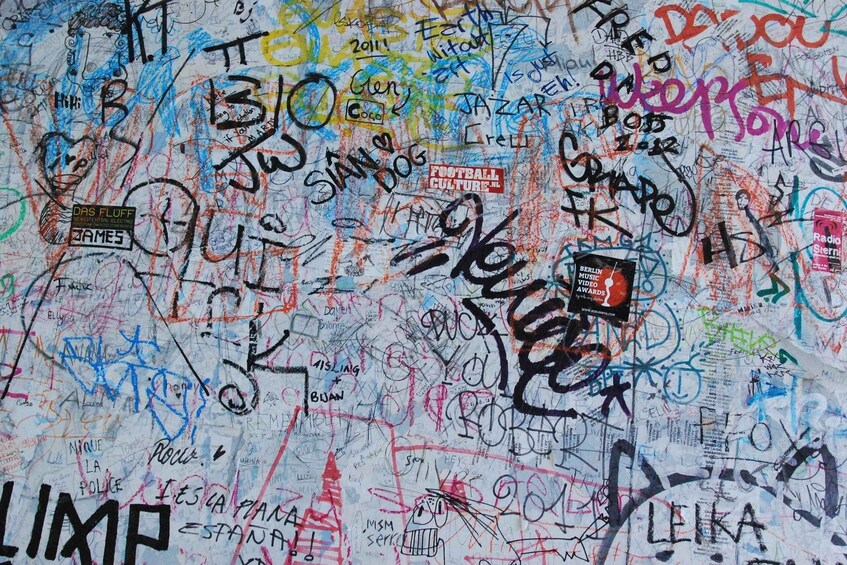A wall covered with various graffiti and stickers, including names and logos. 5