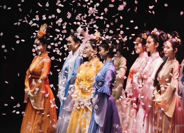 A group of people in traditional costumes with flower petals falling around them. 1