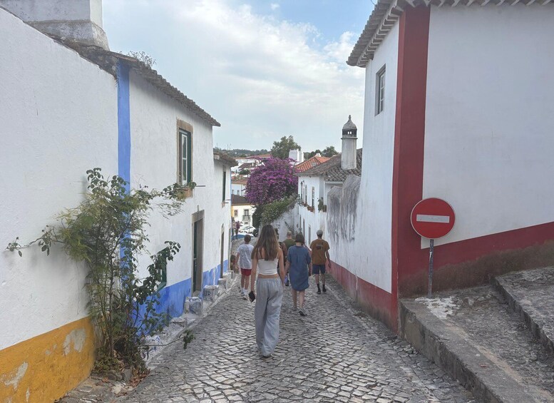 A cobblestone street with white buildings, a red and white wall, and a no-entry sign. 4