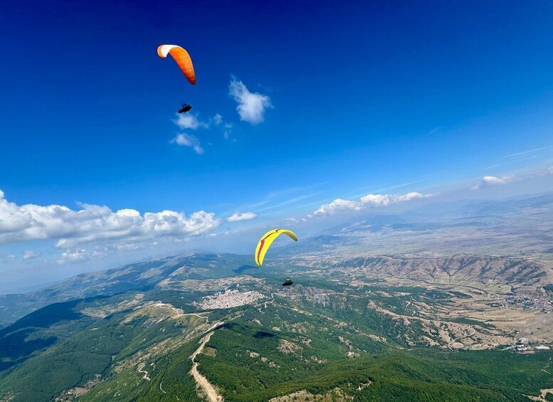 Paragliders flying over a mountainous landscape with a clear blue sky. 2