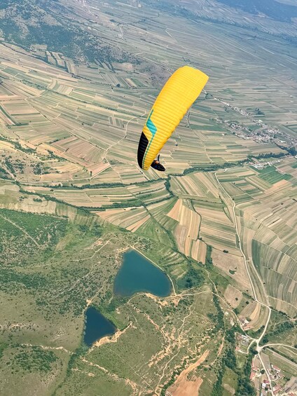 A paraglider flying over a patchwork of agricultural fields and a lake. 3