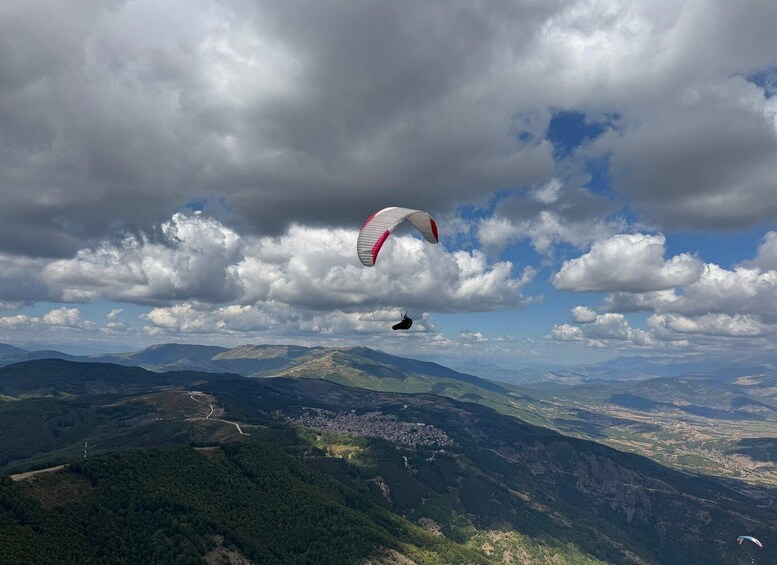 A paraglider flying over a mountainous landscape with a town below. 1
