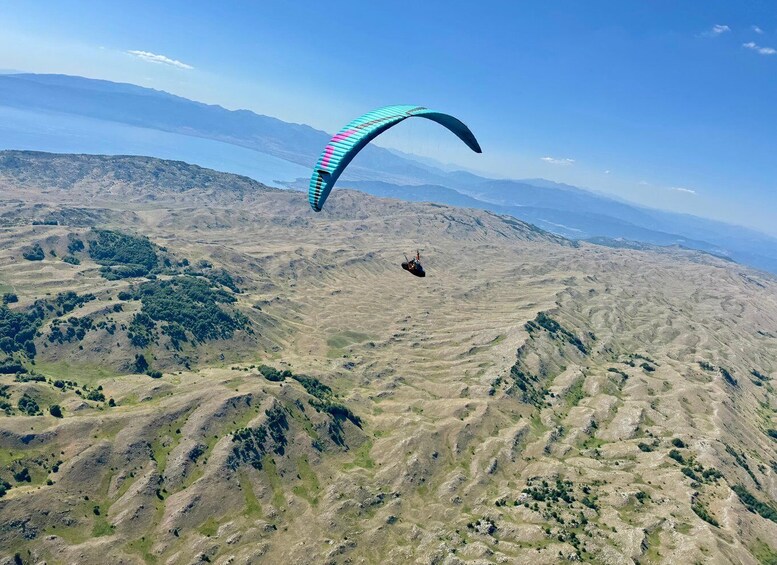 A paraglider flying over a hilly landscape with sparse vegetation. 5