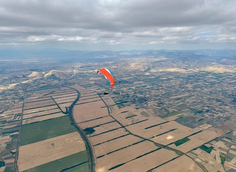 A paragliding scene over agricultural fields with distant mountains. 4