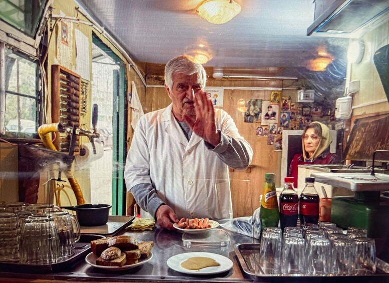 A man in a white coat preparing food at a counter with various dishes, glasses, and bottles. 1