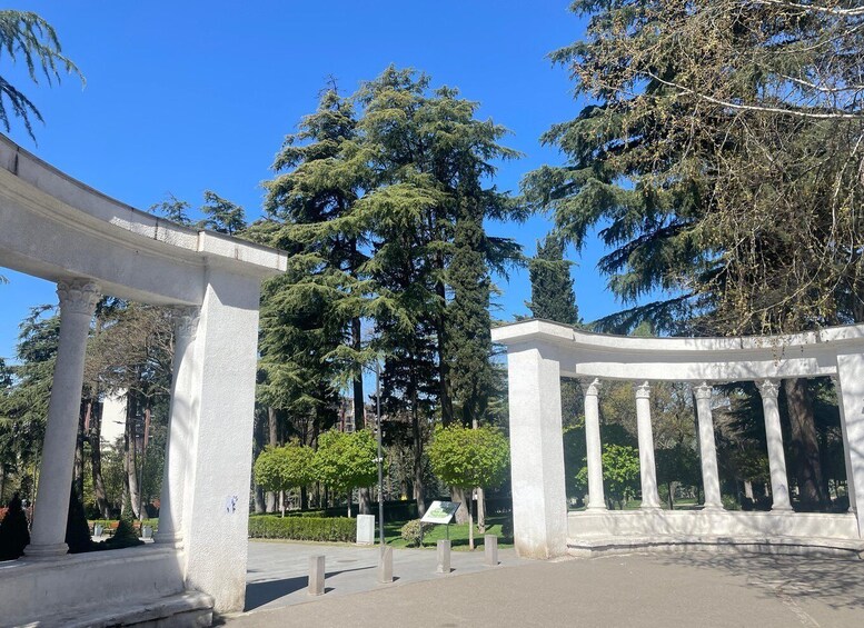 A white arched structure with columns, surrounded by trees and greenery. 2
