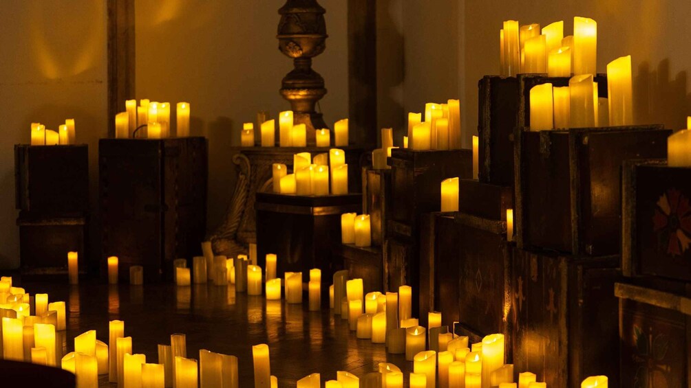 A room filled with numerous lit candles arranged on wooden stands and tables. 5