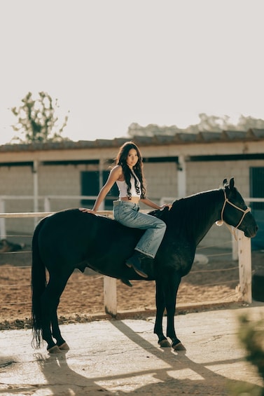 A person sitting on a horse in an indoor stable. 3