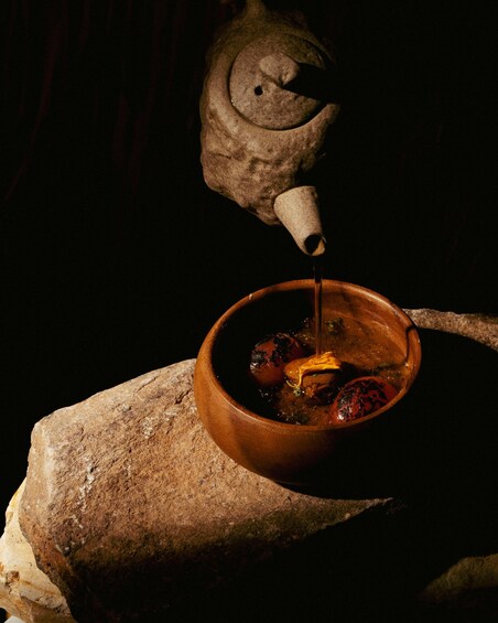 A clay pot with food and a teapot pouring liquid into it. 5