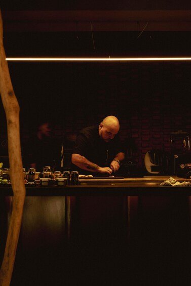 A person working at a counter in a dimly lit kitchen with a brick wall background. 4