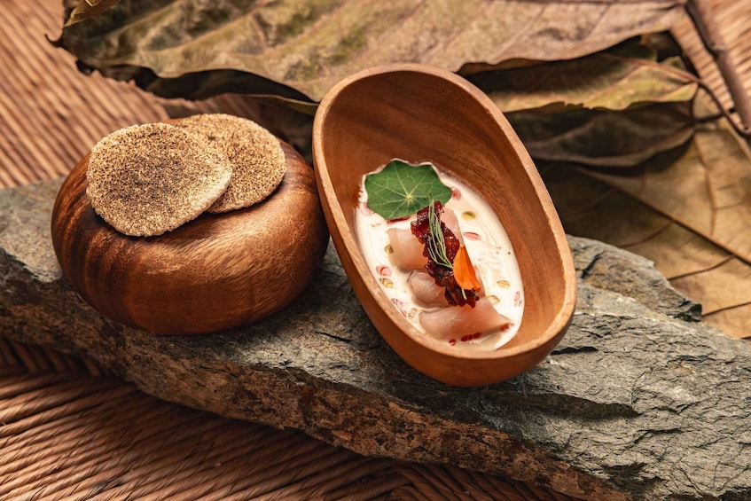 A wooden bowl with a creamy substance and a leaf garnish, placed on a wooden surface with a rustic background. 3