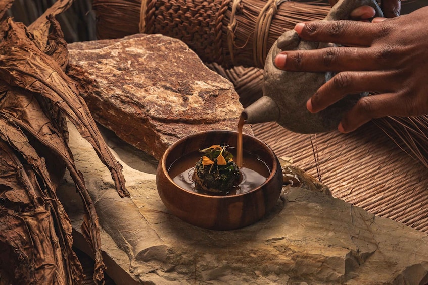 A person pouring liquid from a metal pitcher into a wooden bowl with a plant. 2