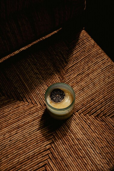A glass of coffee with a slice of black fruit on the rim, placed on a woven mat. 3