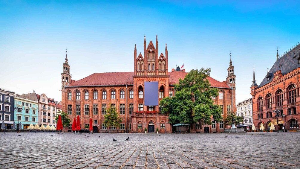 A historic building with a red brick facade and a large central tower, surrounded by cobblestone streets and traditional European architecture. 5
