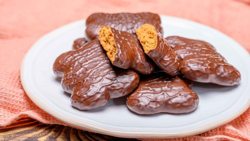 A plate of chocolate-covered cookies with a white background and a pink cloth underneath. 1