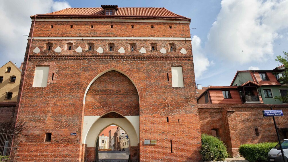 A brick archway with a tiled roof, leading into a narrow street. 4