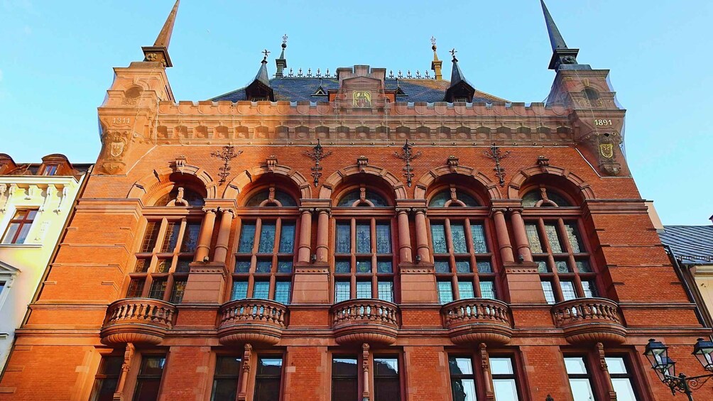 A red brick building with ornate architectural details, including arched windows and a balcony with a balustrade. 2