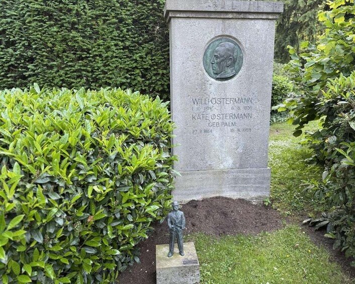 A memorial plaque with inscriptions, a statue, and lush greenery. 3