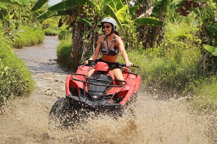 A person riding a red ATV through a muddy path surrounded by greenery. 3