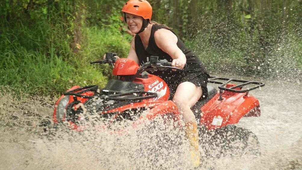 A person riding a red ATV through a body of water. 4