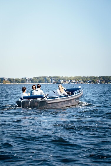 A small motorboat with four people on the water, surrounded by a calm sea and a distant shoreline with buildings. 3