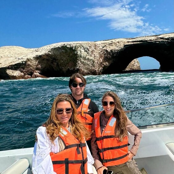 Three people on a boat with life jackets, a rocky coastline, and a natural arch formation in the background. 3