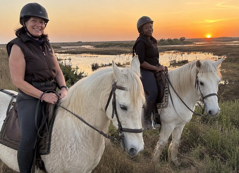 Two people riding white horses in a grassy field with a sunset in the background. 4