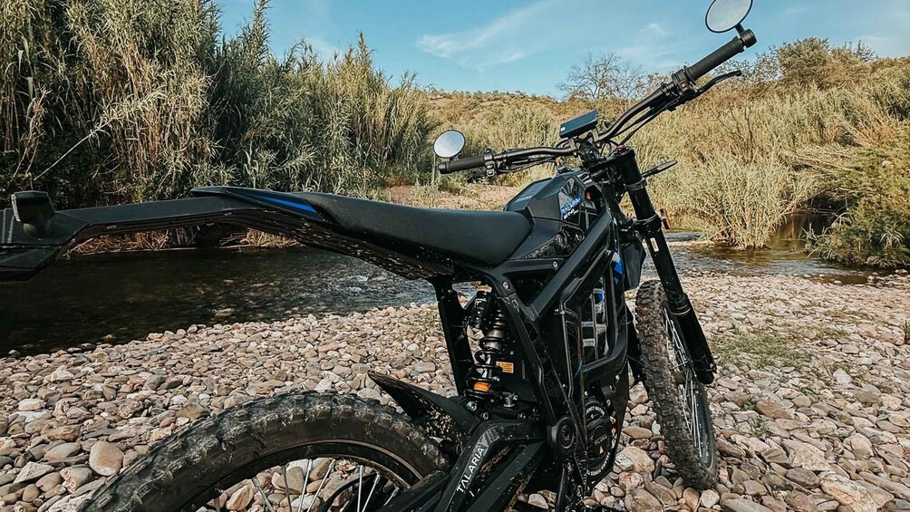 A black off-road motorcycle parked on a rocky riverbed with a clear blue sky in the background. 5