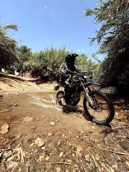 A person on a dirt bike navigating a rocky, muddy trail surrounded by dense vegetation. 4