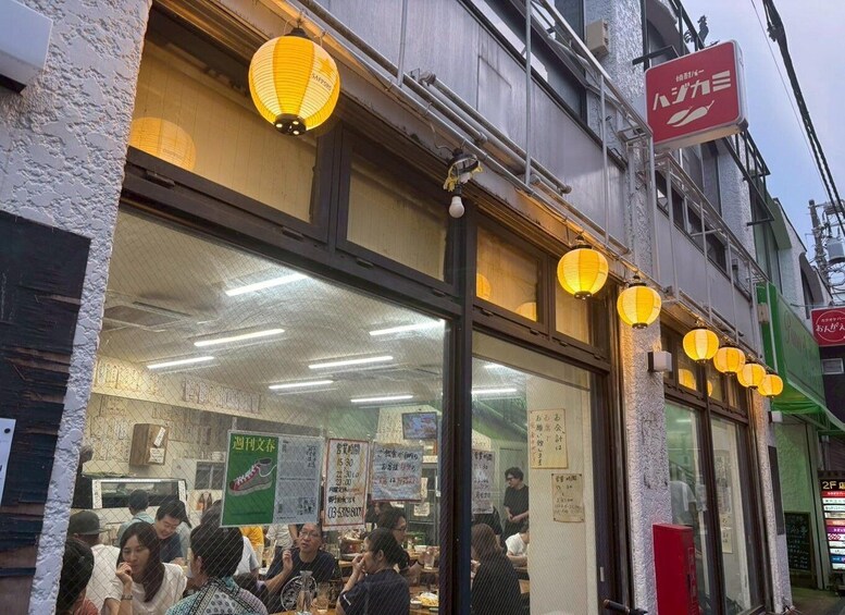 A restaurant with yellow paper lanterns, a signboard, and people dining inside. 4