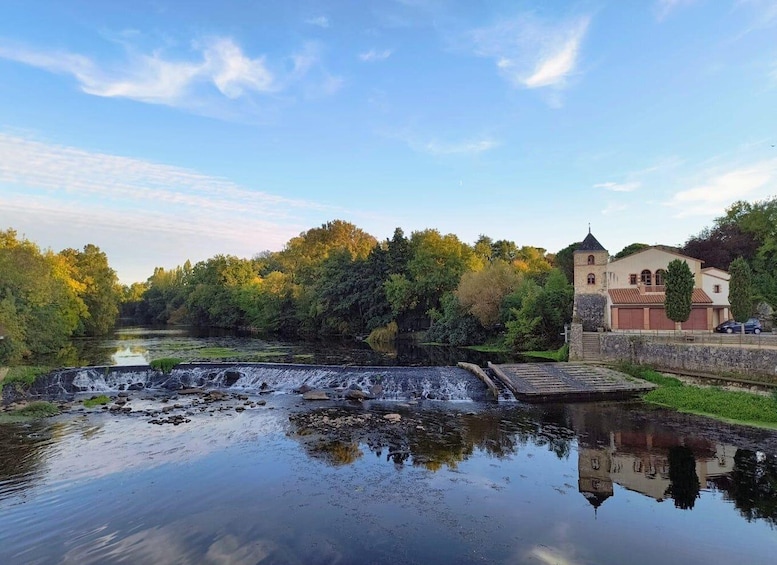 A river with a waterfall, a bridge, and a building with a tower. 5