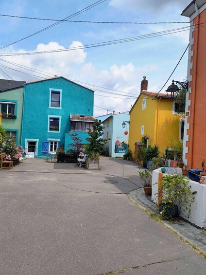 A narrow street with colorful buildings, a mural, and potted plants. 4