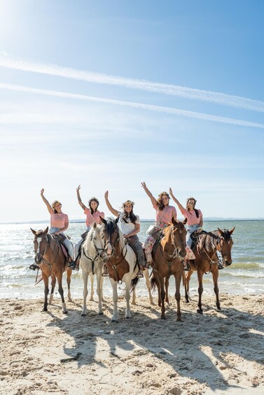 A group of people riding horses on a beach with the ocean in the background. 1