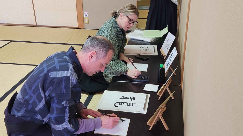 Two people practicing calligraphy at a table with ink bottles and brushes. 3