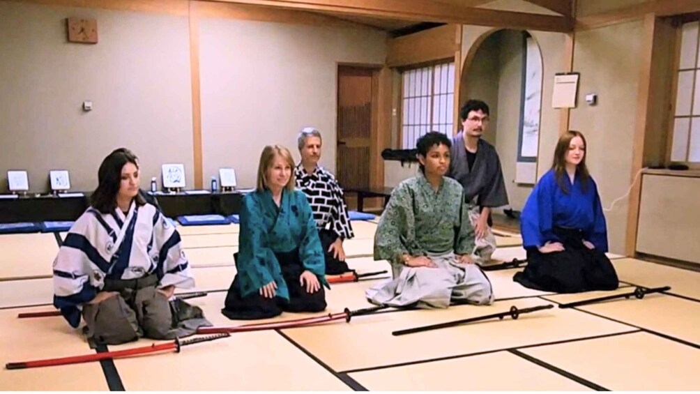 A group of people sitting on tatami mats in a room with a traditional Japanese aesthetic, including shoji screens and a low wooden ceiling. 1