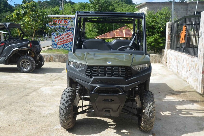 A Polaris off-road vehicle parked on a concrete surface with a building and trees in the background. 3