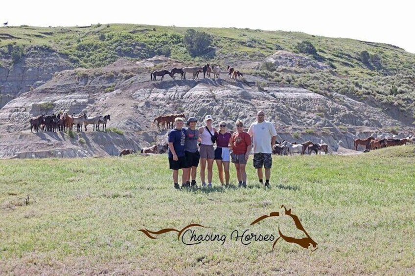 A group of people standing on a grassy hill with horses in the background. 5