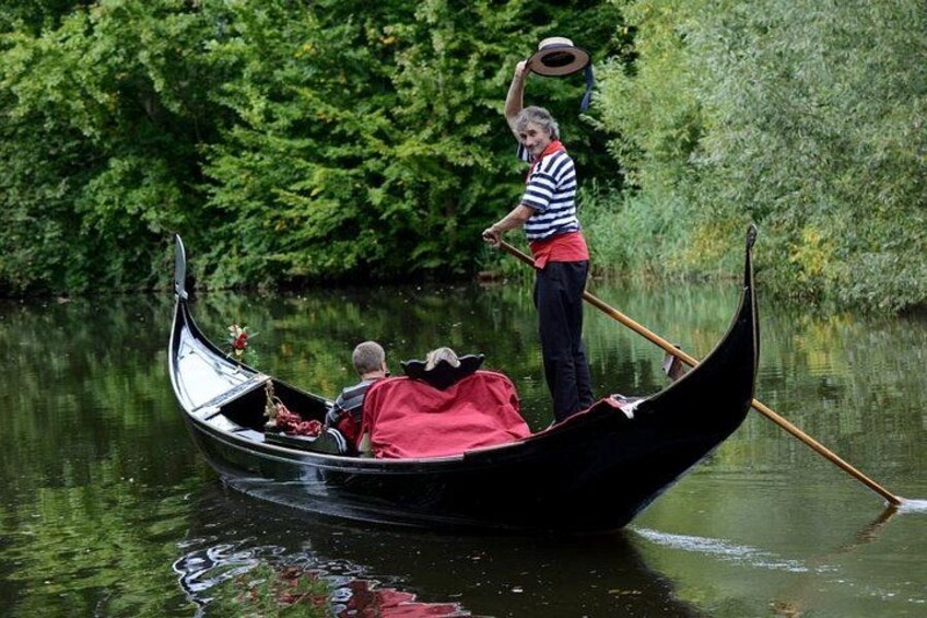 A gondola on a river with a person standing at the stern and another seated inside. 3