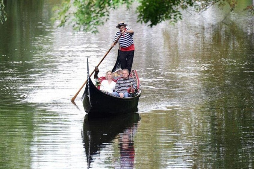 A gondola with a person rowing, passengers, and a river. 1
