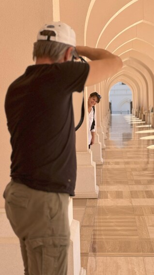 A person taking a photograph in a corridor with a tiled floor and arched ceilings. 2