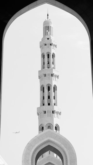 A tall, white minaret with intricate designs and a dome at the top, viewed through an arched window. 5